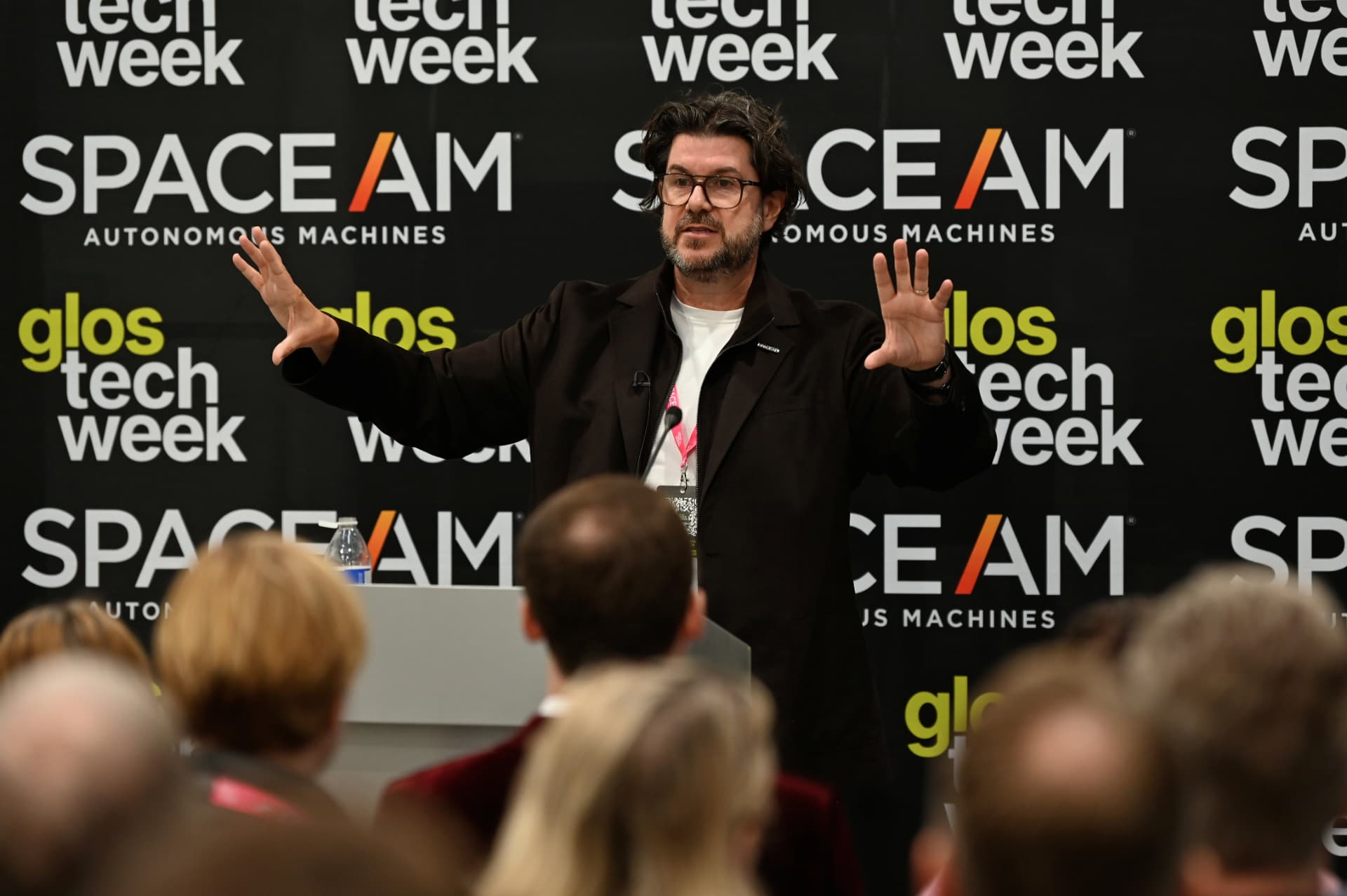 Speaker gesturing at a lectern in front of an audience at Gloucestershire Tech Week